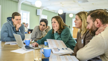 Personer sitter i gruppearbeid ved bord og ser på PC