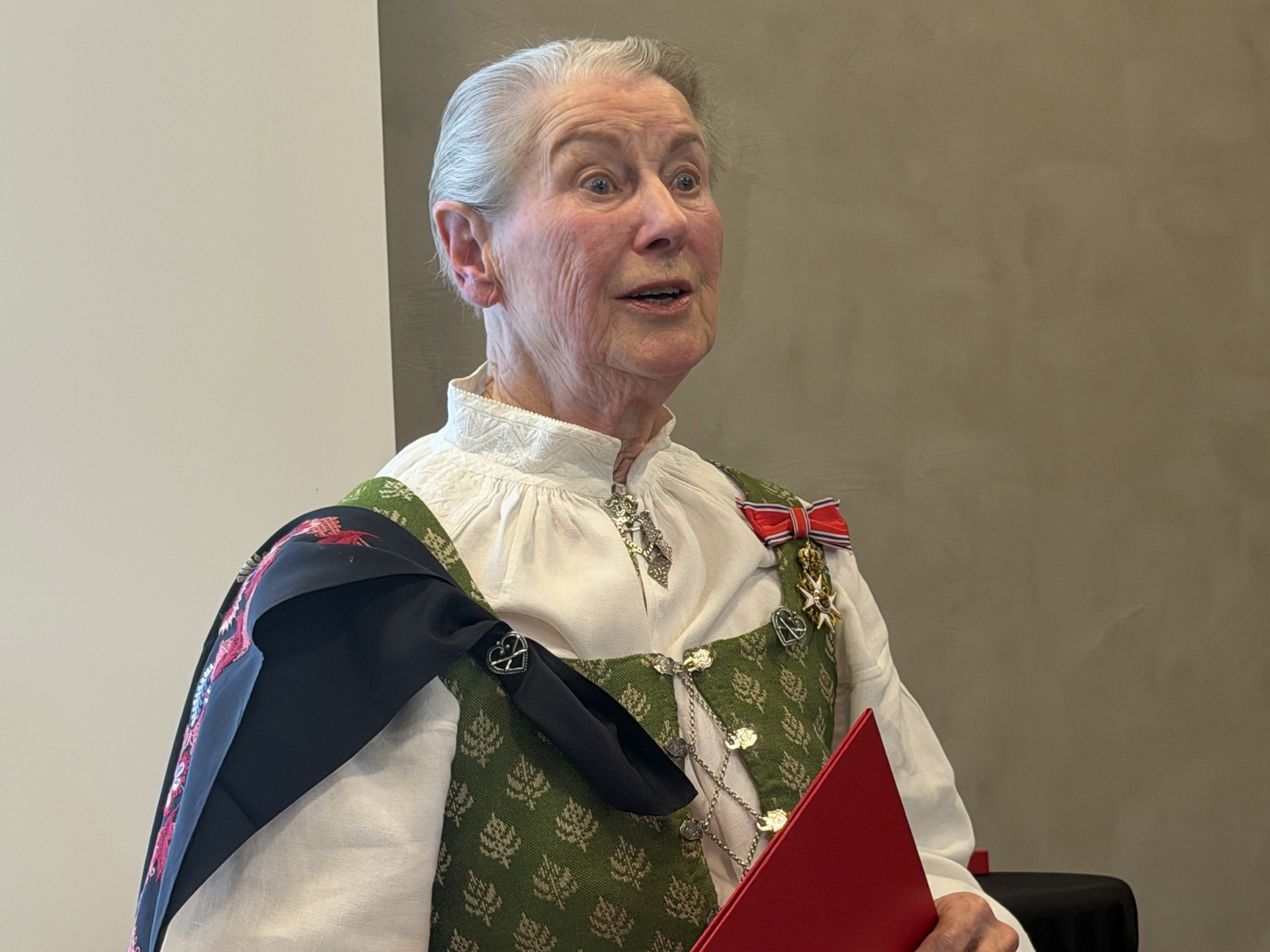 Bilde av Kirkengen fra overrekkelsen. Hun har grått, kortklippet hår, og har på seg bunad. Denne har hvit skjorte, sølje i halsen, sort sjal med broderte blomster i rødt og rosa, og bunadsvesten er lysgrønn med sølvknyting i front. På venstre skulder henger dekorasjonen hun er tildelt: En rød sløyfe med hvitt og blått i kantene, og en gullstjerne. Hun holdet på en rød mappe. 