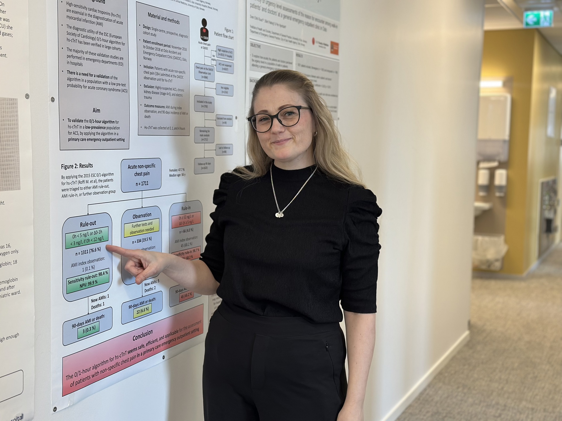  ph.d. Tonje R. Johannessen, forsker og legeskiftleder ved Allmennlegevakten i Oslo peker på poster i korridoren