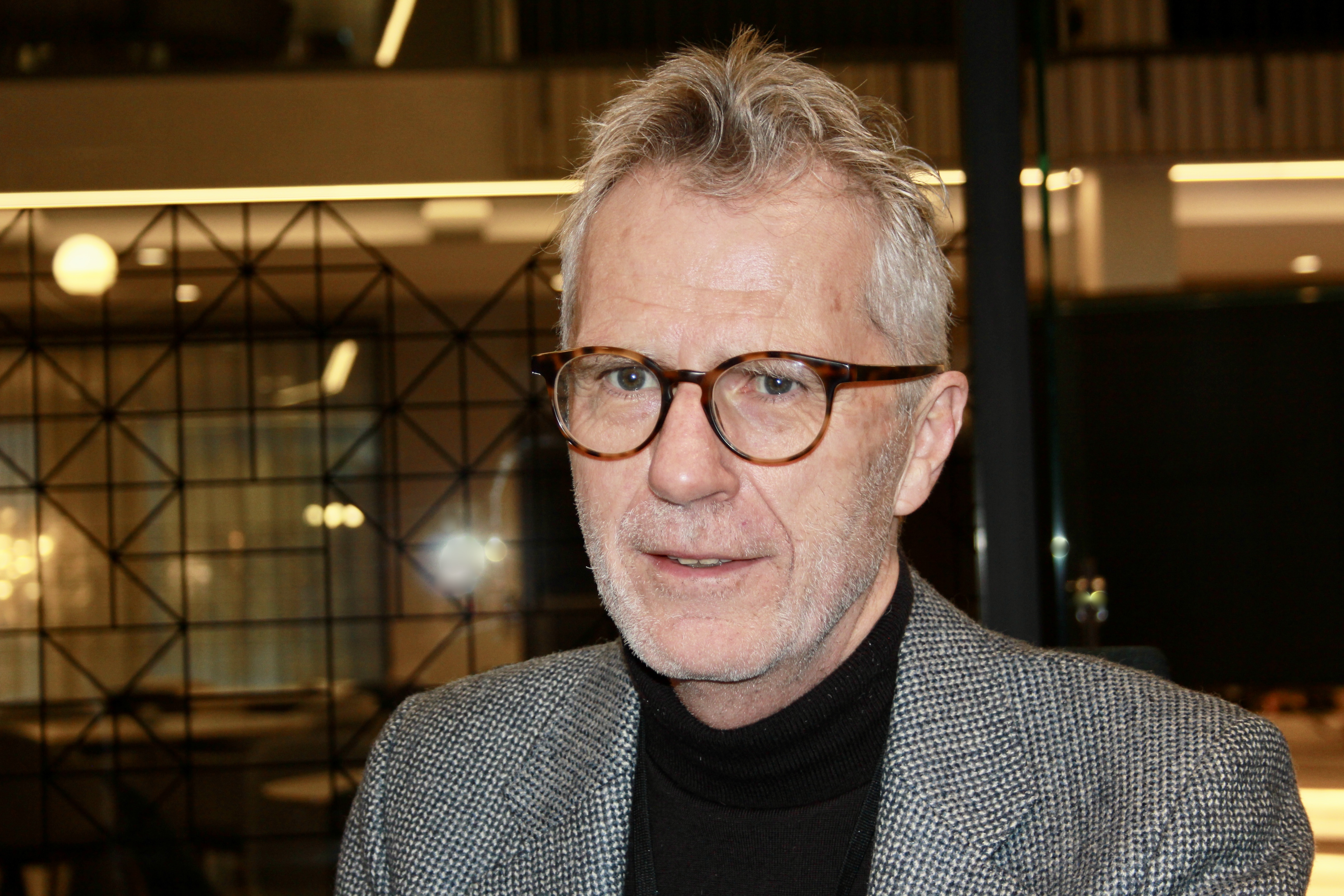 Mann, gr&aring;tt h&aring;r, briller, gr&aring; dressjakke og m&oslash;rk genser