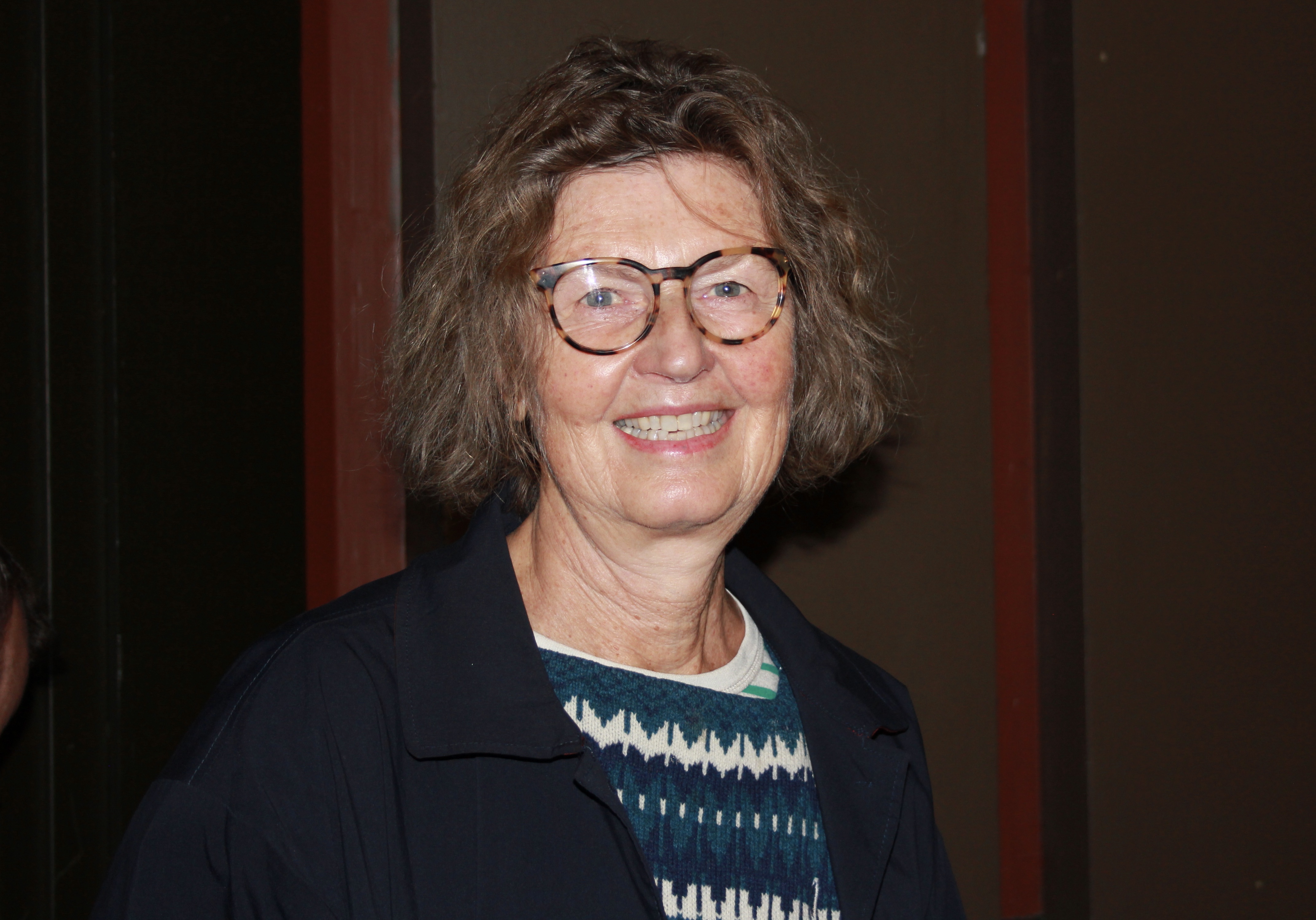 Kvinne med gr&aring;tt kr&oslash;llete h&aring;r som smiler.