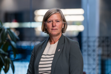 Portrettfoto av legepresident Anne-Karin Rime. Utsnittet er fra livet og opp. Bakgrunnen er uskarp. Rime har lyst hår til rett under ørene, og hun har sideskill. Håret er bak ørene. Hun har perleøredobber. Hun har på seg grå dressjakke med en Legeforeningen-pin på jakkeslaget, og inni dressjakka har hun en hvit genser med grå striper.