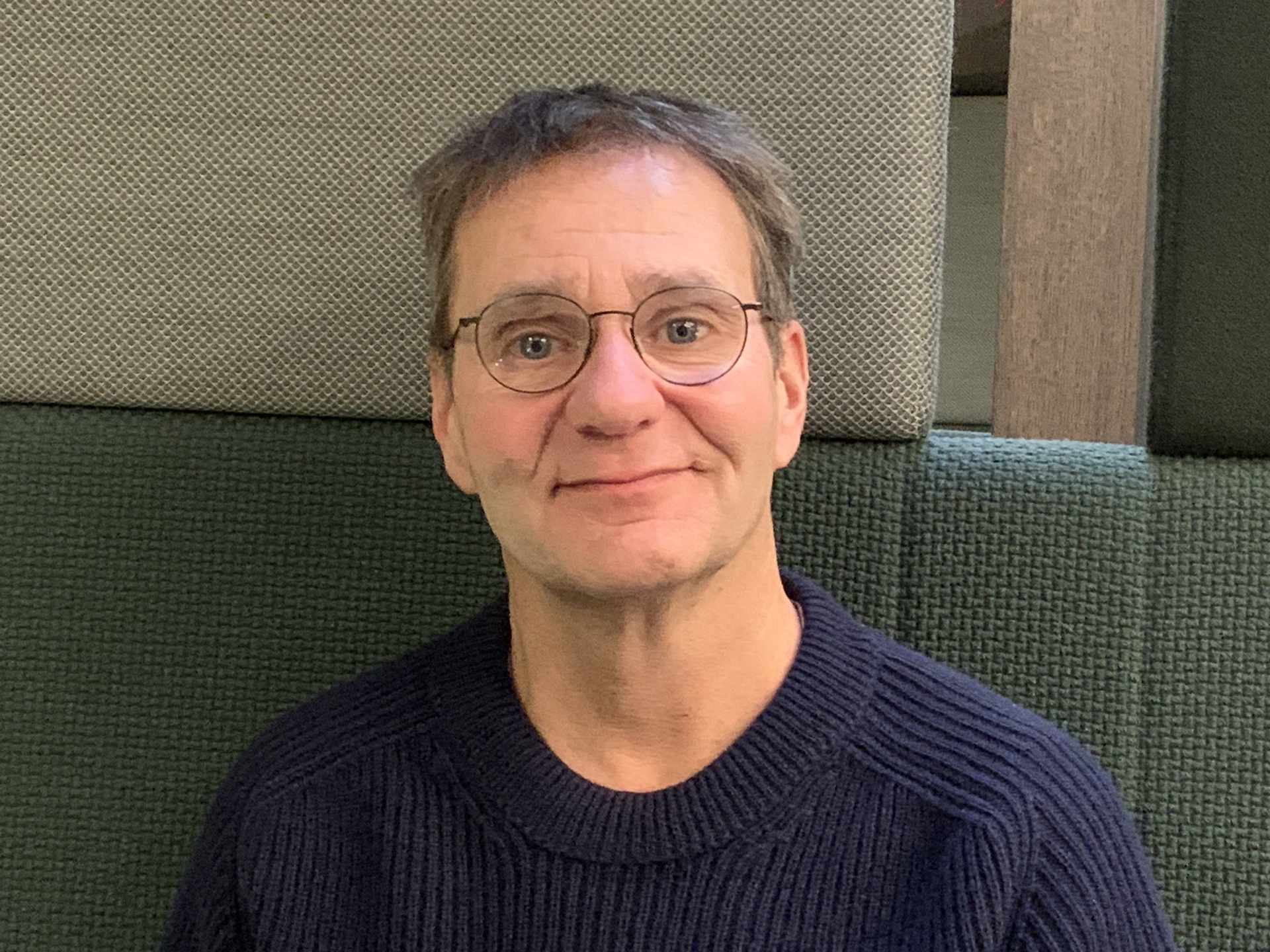 Mann med kort hår og briller. Blå genser. Grønn og beige bakgrunn.