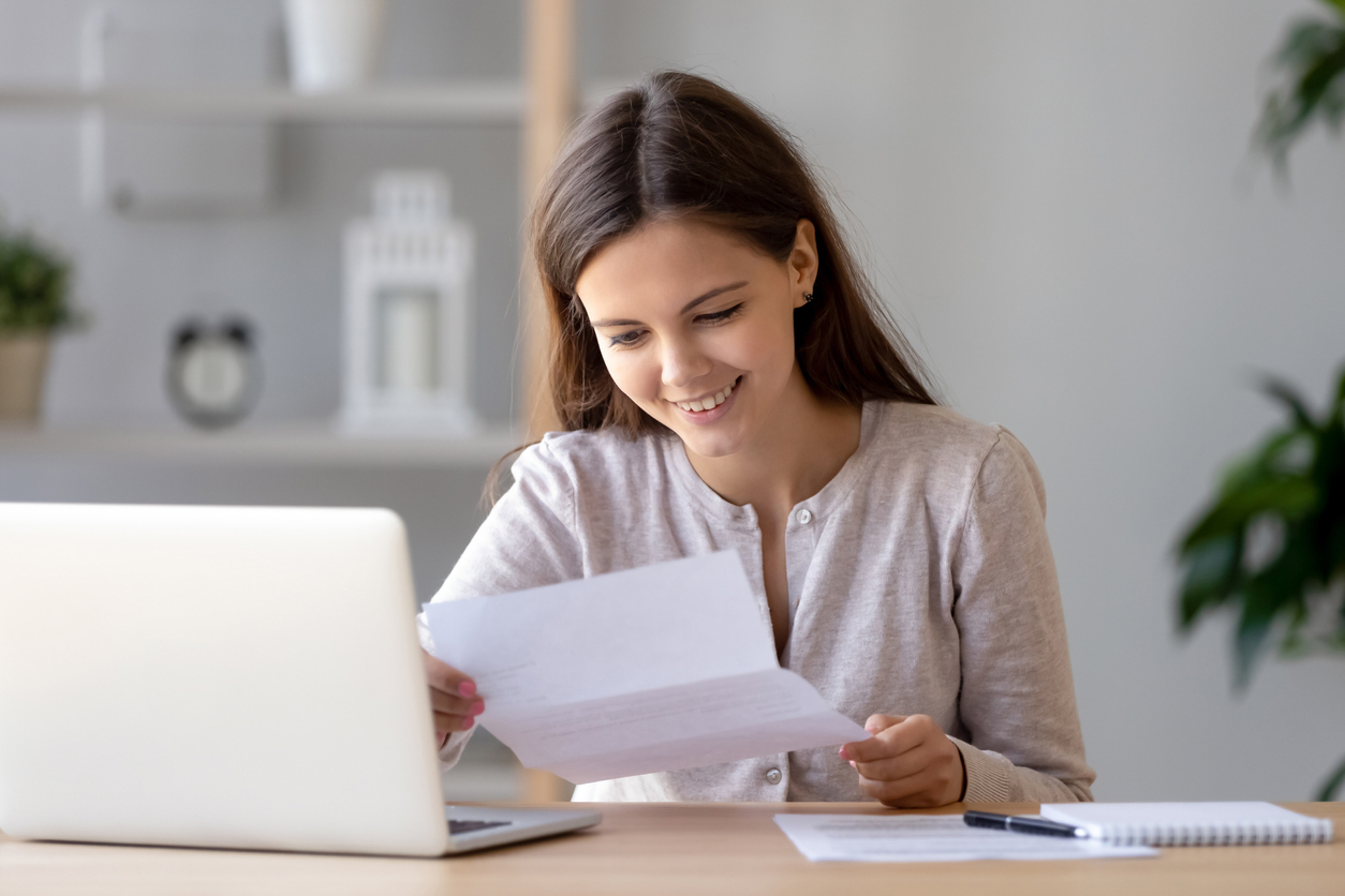 Kvinne som smiler mens hun leser et ark foran en pc. Foto: Istockphoto.com