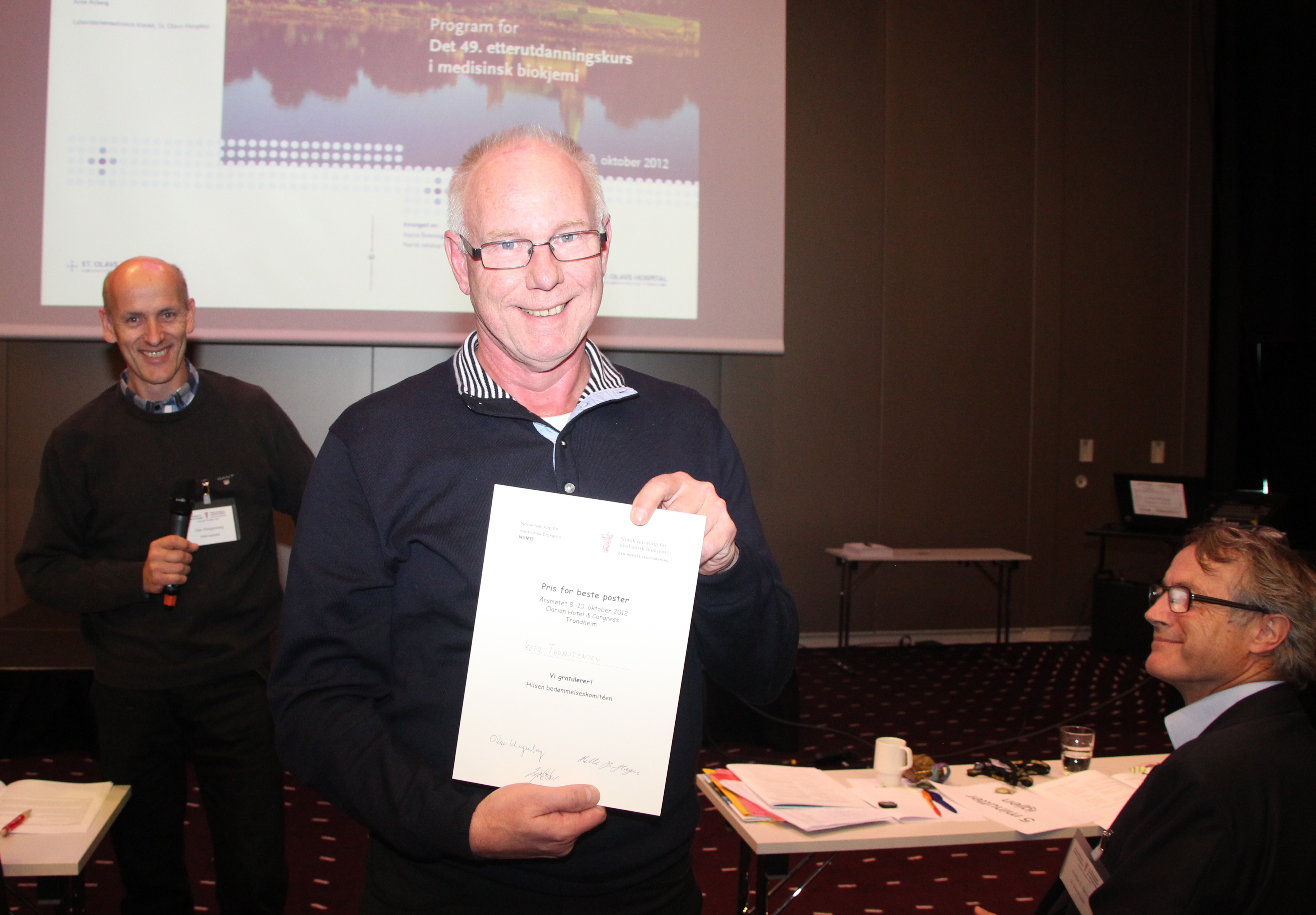 Prisen for beste poster gikk til Ketil Thorstensen ( i bakgrunnen sees prisutdeler og leder av NFMB, Olav Klingenberg og til høyre kursleder Kristian Bjerve). Foto: Helle B. Hager