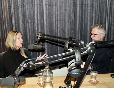 Kvinne med lyst hår og svart genser. Mann med grått hår, briller og svart genser. Bak mikrofonstativer. Grå fløyelsgardiner bak.