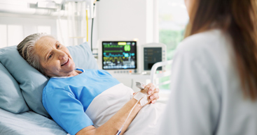 En gammel dame ligger i en sykeseng og smiler til en lege. Foto: Istockphoto.com/Jacob Wackerhausen