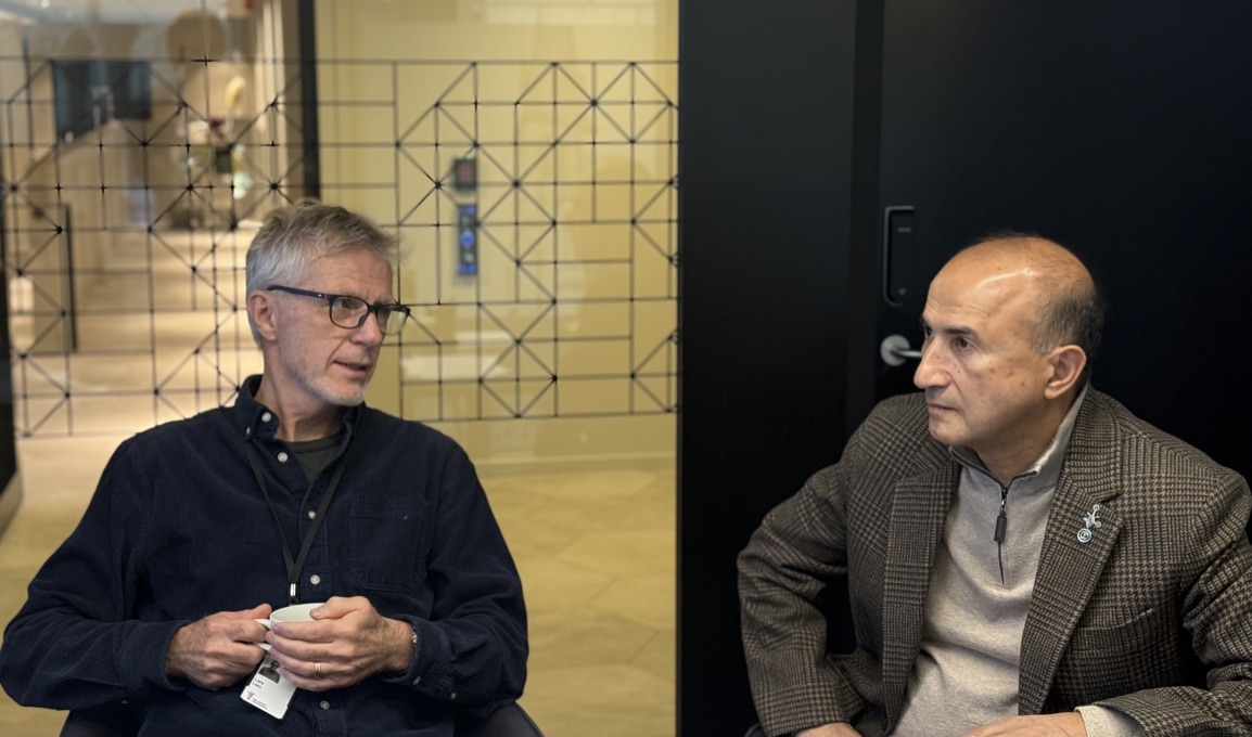 To menn som snakker sammen. Til venstre en mann med gr&aring;tt h&aring;r, briller og m&oslash;rk genser. Til h&oslash;yre, en mann med brun genser og jakke.