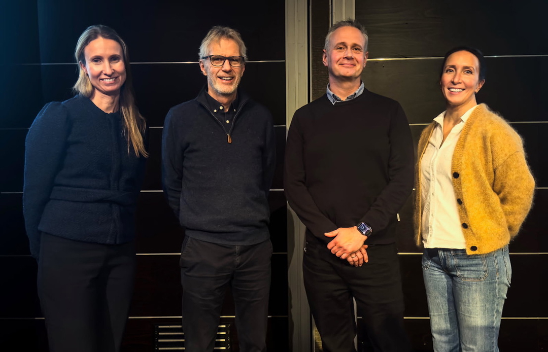 En kvinne i mørke klær, to menn i mørke klær og en kvinne i lys topp og gul jakke. Mørk bakgrunn.