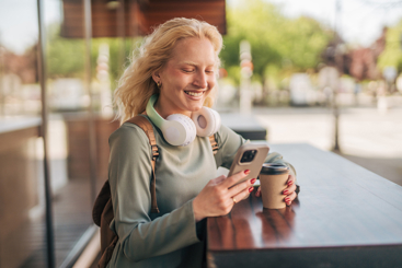 En kvinne som sitter ved et bord med en kopp kaffe og en mobiltelefon. Foto: Akademikerne pluss