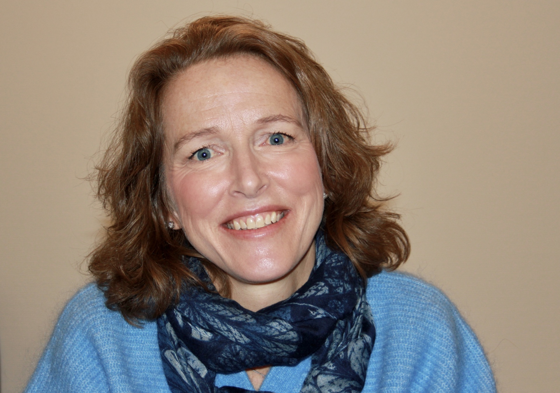 Smilende kvinne med halvlangt blondt hår. Lyseblå genser. Blått skjerf om halsen.