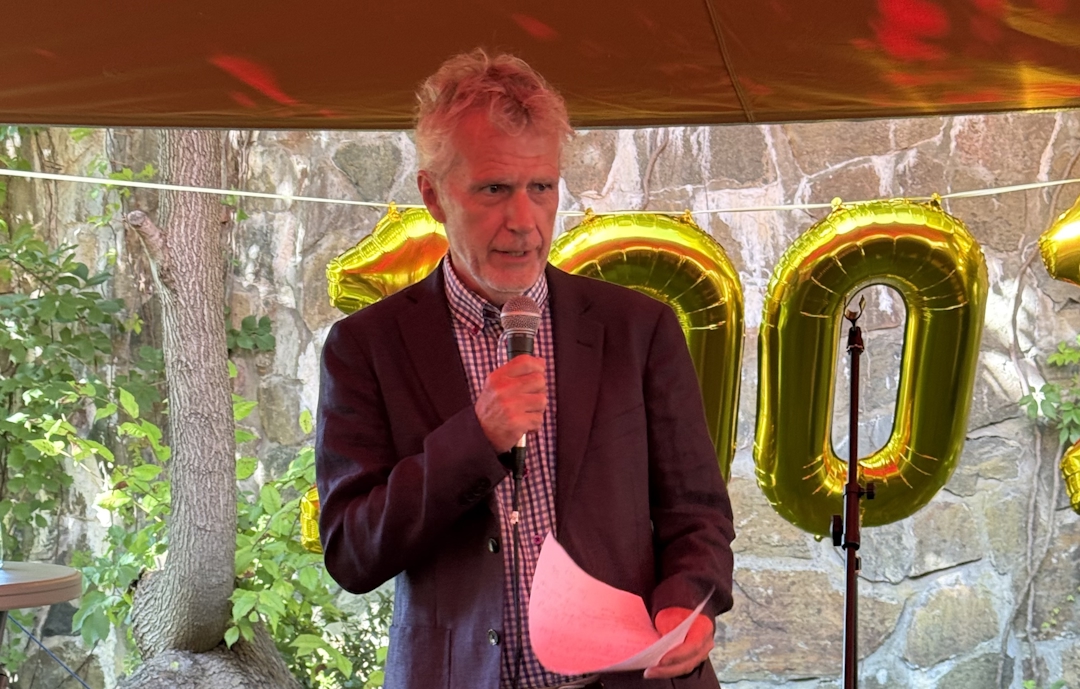 Mann med svart jakke og mikrofon i et telt, utendørs.