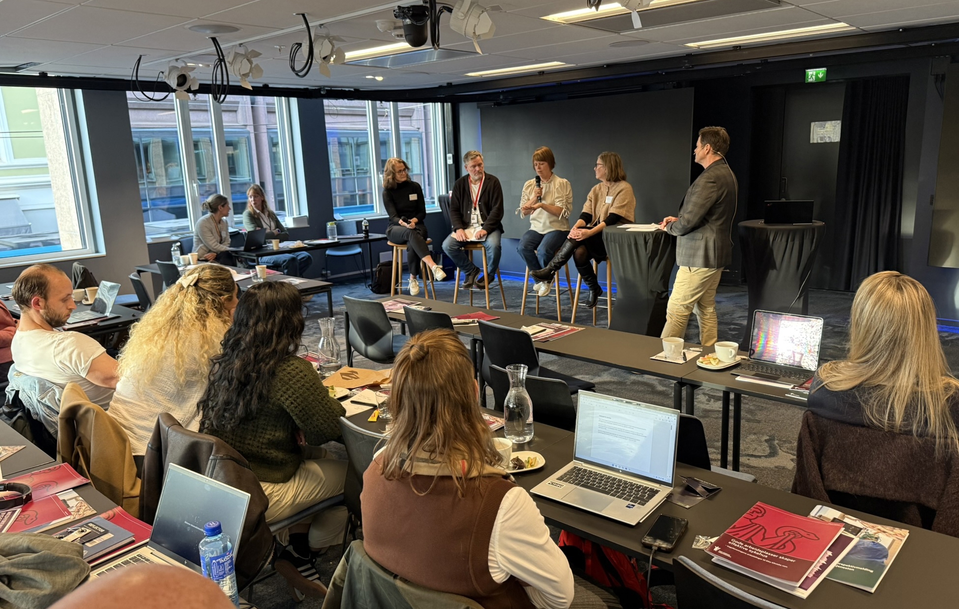 Bilde av bidragsyterne i panelsamtalen. Panelet sitter på høye barkrakker. Foran dem sitter deltakerne på kurset som vi ser bare rygger og bakhoder på. Panelet fra venstre: Hildegunn Borkamo, tidligere tillitsvalgt Helse Førde. Hun har bølgete hår til skuldrene, briller, sort genser og jeans. Hun holder en mikrofon i fanget. Oddvar Synnes, foretaksverneombud OUS. Han har grått, kortklippet hår, sort cardigan med hvit t-skjorte inni og jeans. Zuzana Huncikova, foretakstillitsvalgt Stavanger universitetssykehus. Hun har kortklippet, rødbrunt hår, hvit skjorte og jeans. Hun snakker i en mikrofon. Kari Jøssang, prosjektdirektør nye Stavanger universitetssykehus. Hun har halvlangt, brunt hår, beige genser og jeans. Hun har bena krysset og holder hendene på ene kneet. Ståle Clementsen var orstyrer. Han står til høyre i bildet, og vi ser ham fra siden. Han har kortklippet, brunt hår, grå dressjakke og lyse bukser. 